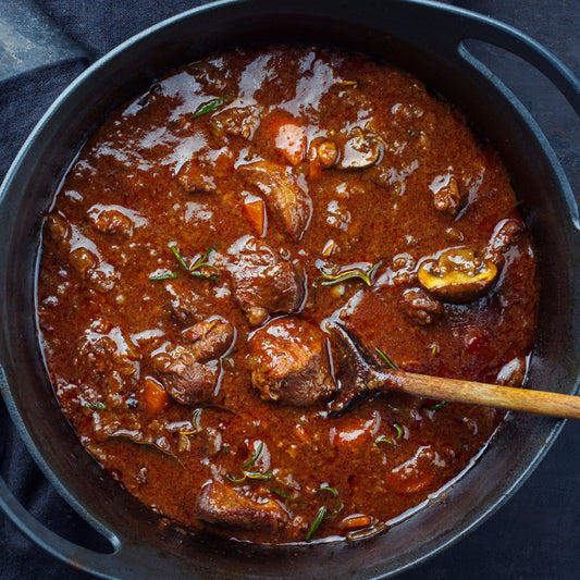 Mixed Game Meat Stew with vegetables in a dark pan with a wooden spoon