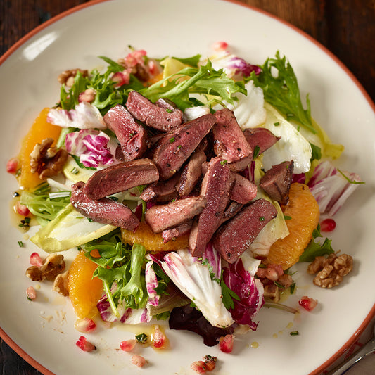 Salad with sliced meat, oranges, and nuts on a white plate.