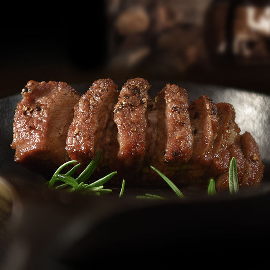 Sliced wild boar meat cooked with rosemary on a dark surface