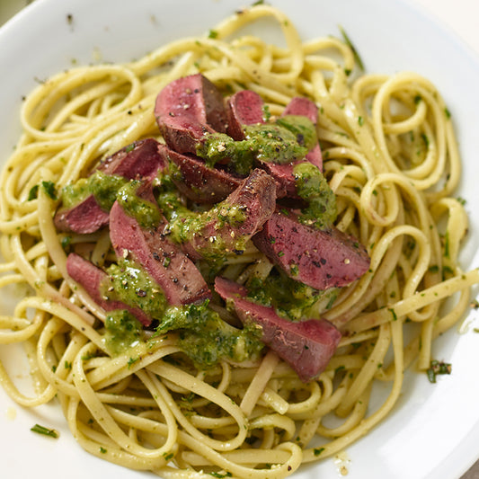 Wood pigeon Spaghetti with green sauce and sliced meat on a white plate