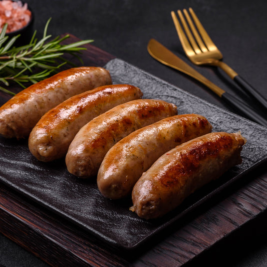 cooked venison and cranberry sausages on a black slate plate with rosemary and gold cutlery.