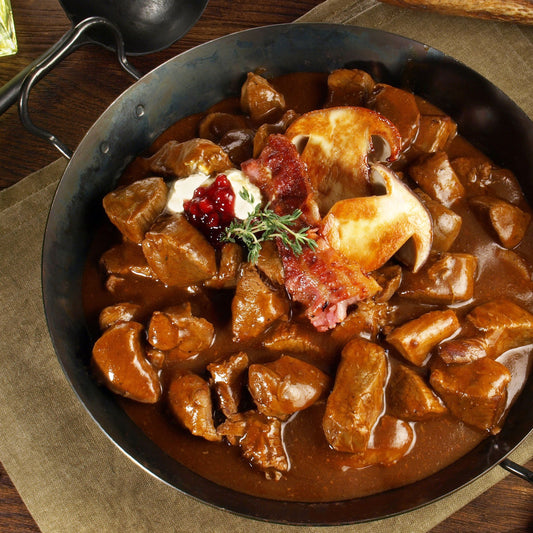 Diced game meat Stew in a pan with a garnish on a wooden table