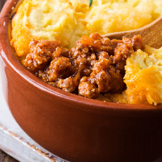 Terracotta bowl with minced venison shepherd's pie on a white background