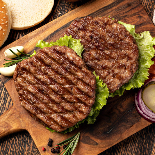 Two grilled wild boar and apricot hamburger patties on a wooden cutting board with lettuce and garnishes.
