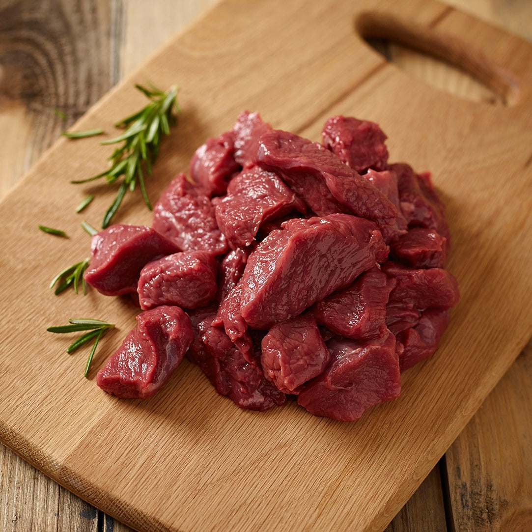 Raw diced venison chunks on a wooden cutting board with rosemary sprigs.