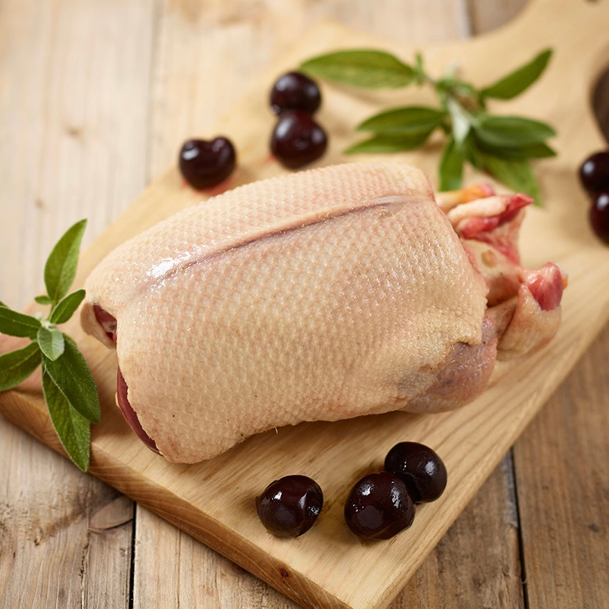 Raw duck on a wooden cutting board with olives and olive branches