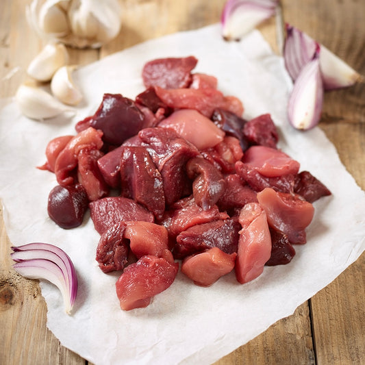 Raw diced mixed game meat on a paper towel with garlic and onions on a wooden surface