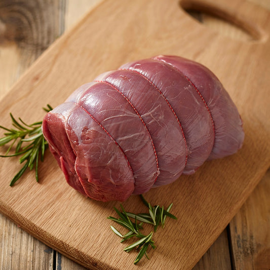 Venison haunch meat boned and rolled on a wooden cutting board with rosemary