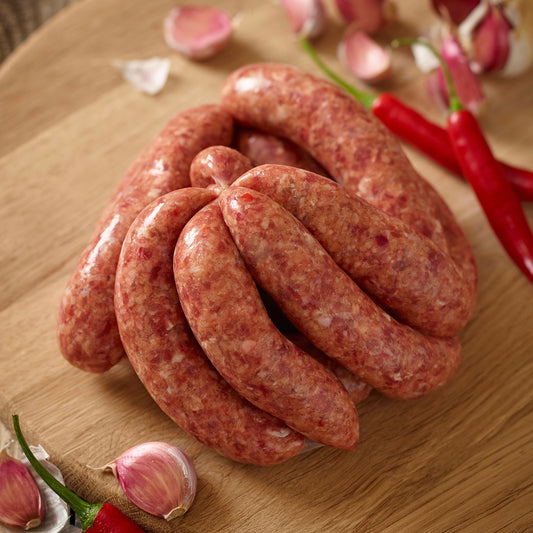 Raw wild boar chilli and garlic sausage link on a wooden board with red peppers and garlic cloves.